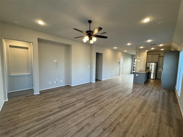 unfurnished living room with baseboards, wood finished floors, a ceiling fan, and recessed lighting