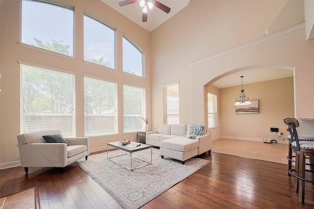 living area featuring arched walkways, ceiling fan, wood-type flooring, baseboards, and a high ceiling