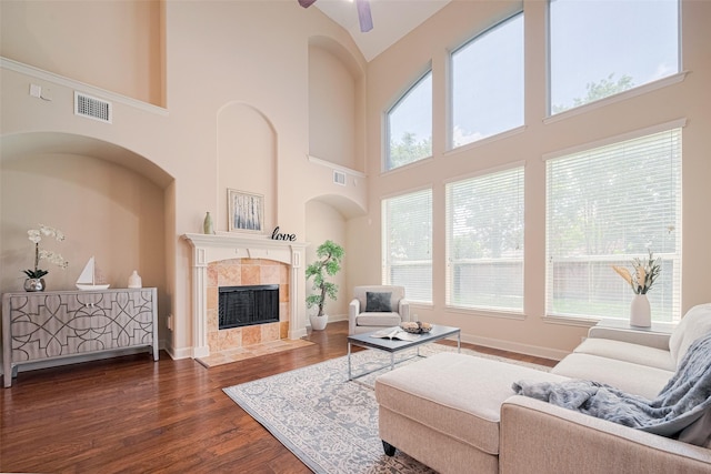 living room with high vaulted ceiling, healthy amount of natural light, dark wood-style flooring, a tiled fireplace, and ceiling fan