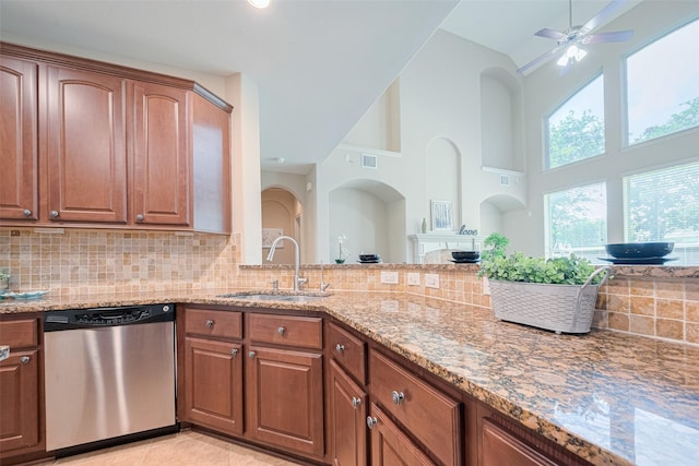 kitchen featuring stainless steel dishwasher, a sink, light stone counters, high vaulted ceiling, and backsplash