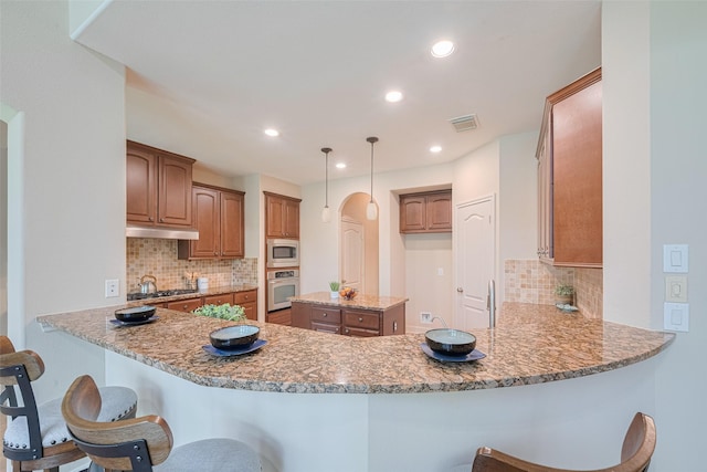 kitchen with stainless steel appliances, under cabinet range hood, decorative backsplash, a peninsula, and recessed lighting