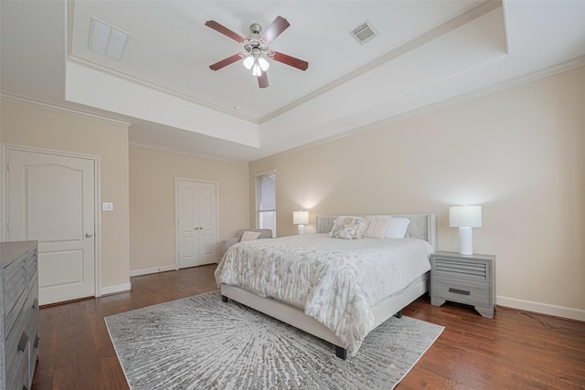 bedroom featuring a raised ceiling, ornamental molding, dark wood-style flooring, baseboards, and ceiling fan