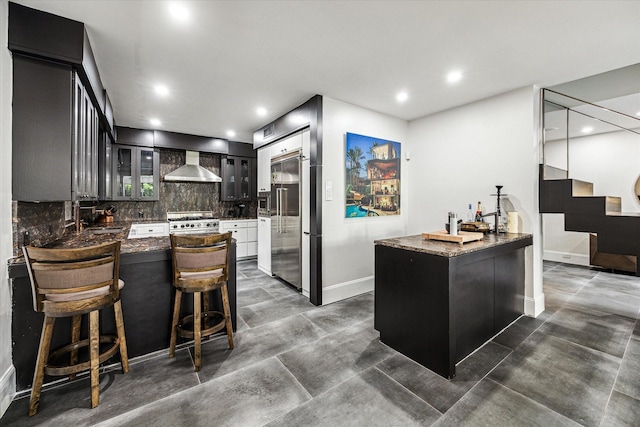 kitchen with wall chimney exhaust hood, high quality appliances, a peninsula, decorative backsplash, and baseboards