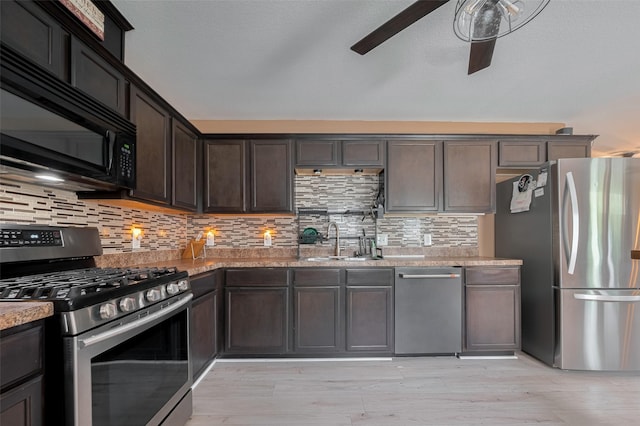 kitchen with appliances with stainless steel finishes, a sink, a ceiling fan, light stone counters, and dark brown cabinetry