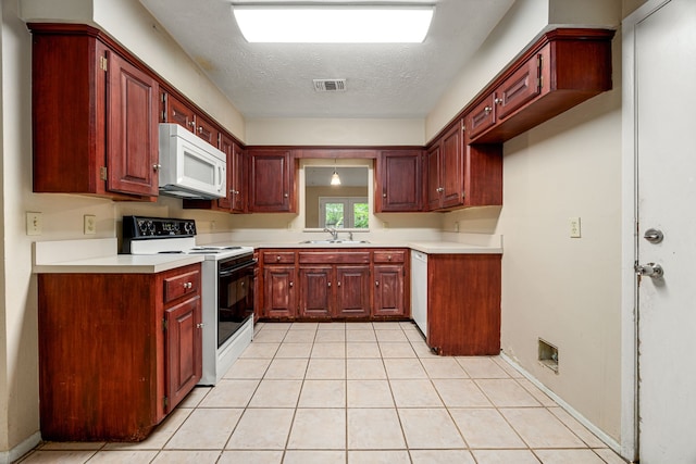 kitchen with white appliances, a sink, reddish brown cabinets, light tile patterned floors, and light countertops