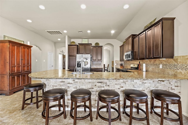 kitchen featuring arched walkways, appliances with stainless steel finishes, a sink, a peninsula, and tasteful backsplash