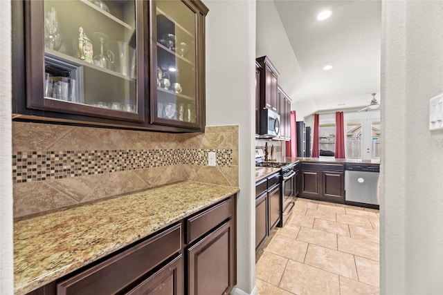 kitchen with appliances with stainless steel finishes, tasteful backsplash, dark brown cabinets, light stone counters, and glass insert cabinets