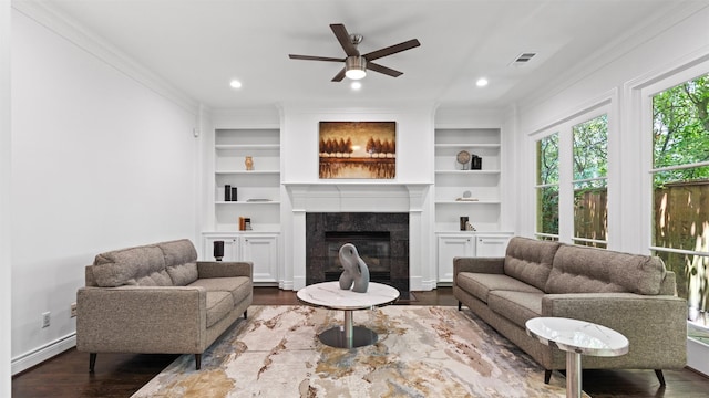 living room featuring crown molding, a ceiling fan, dark wood-style floors, a premium fireplace, and built in features