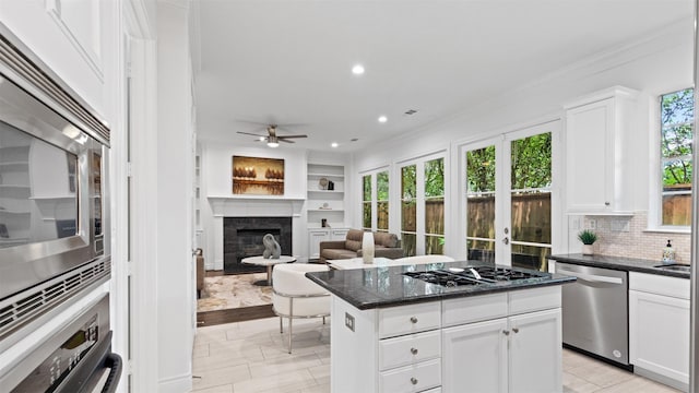 kitchen featuring appliances with stainless steel finishes, ornamental molding, a ceiling fan, a fireplace, and white cabinetry