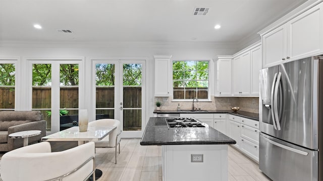 kitchen featuring appliances with stainless steel finishes, a kitchen island, a sink, white cabinets, and backsplash
