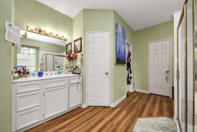 bathroom with wood finished floors, a shower stall, baseboards, and vanity