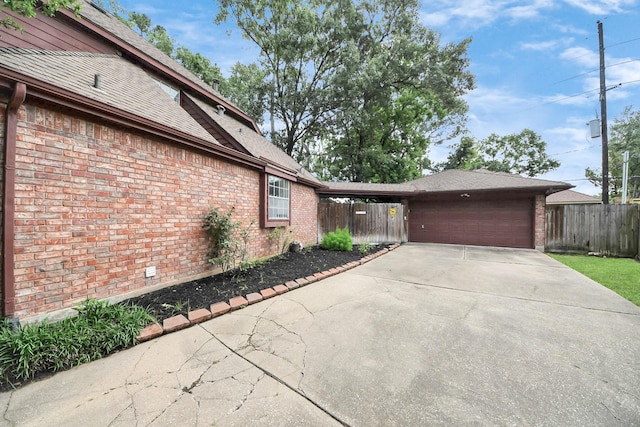 view of property exterior with brick siding, fence, an attached garage, and concrete driveway