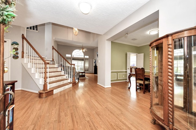 entryway featuring stairs, light wood-style floors, a ceiling fan, a textured ceiling, and ornamental molding