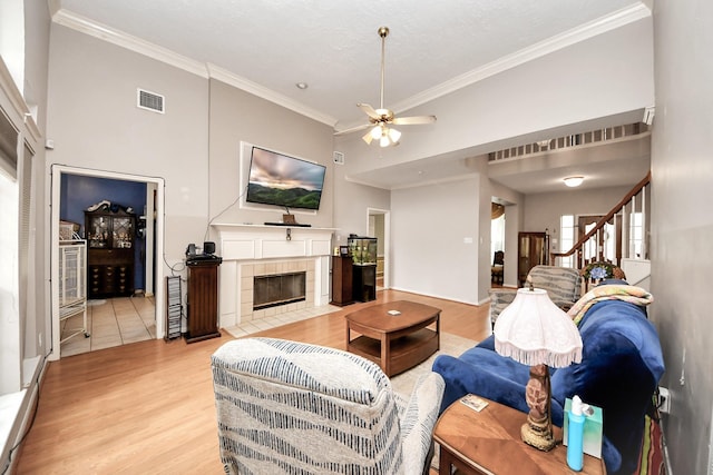 living room with crown molding, ceiling fan, a fireplace, light wood-style floors, and stairway