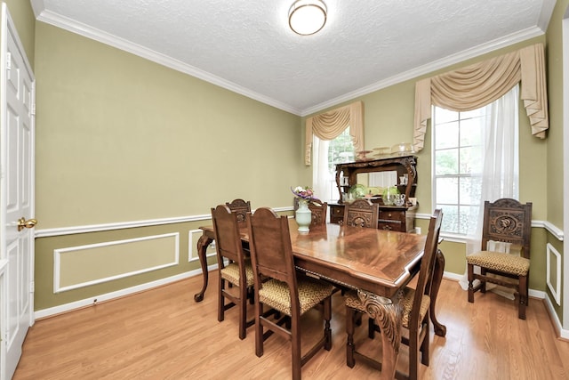 dining area featuring light wood-style flooring, ornamental molding, a textured ceiling, and baseboards