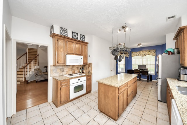 kitchen featuring white appliances, a kitchen island, backsplash, light stone countertops, and a textured ceiling