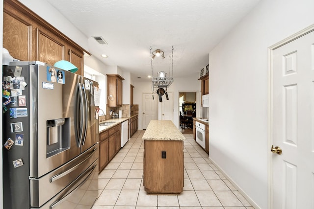 kitchen with white appliances, a center island, light tile patterned flooring, a sink, and light stone counters