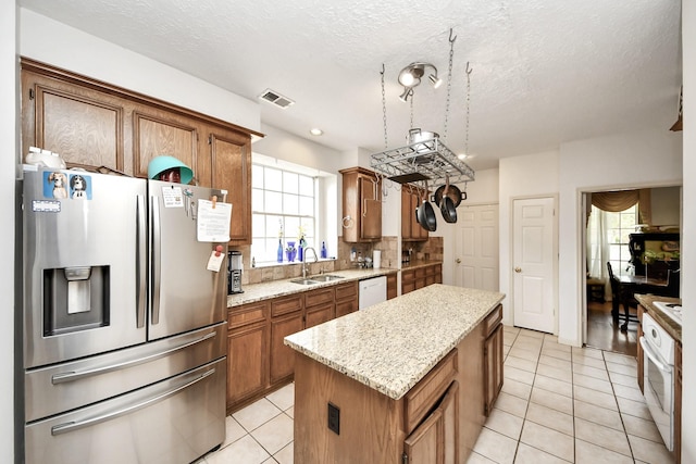 kitchen with white appliances, a sink, a kitchen island, light tile patterned floors, and brown cabinetry
