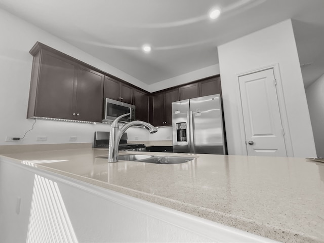 kitchen featuring stainless steel appliances, a sink, dark brown cabinetry, light stone countertops, and recessed lighting
