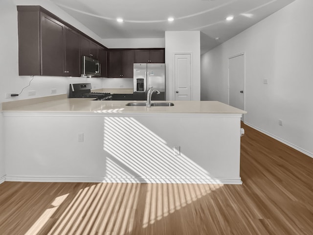 kitchen featuring stainless steel appliances, wood finished floors, a sink, dark brown cabinets, and light countertops