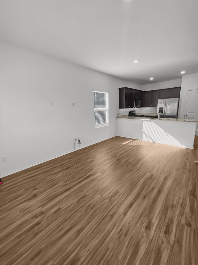 unfurnished living room with wood finished floors, recessed lighting, a sink, and baseboards