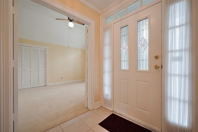 foyer featuring carpet floors, crown molding, a ceiling fan, tile patterned floors, and baseboards