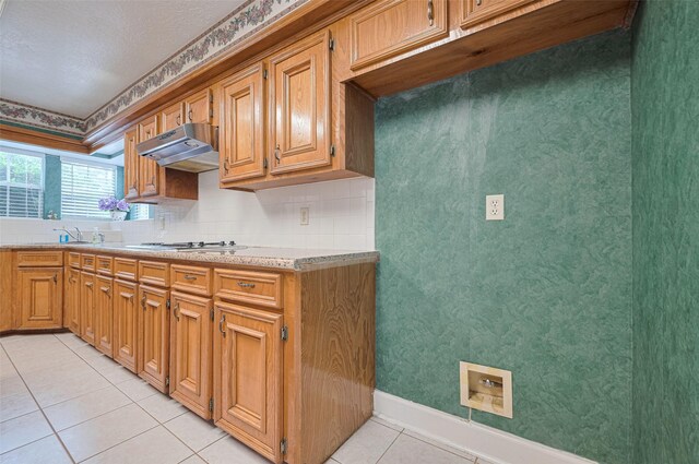 kitchen featuring light tile patterned flooring, light countertops, under cabinet range hood, tasteful backsplash, and baseboards