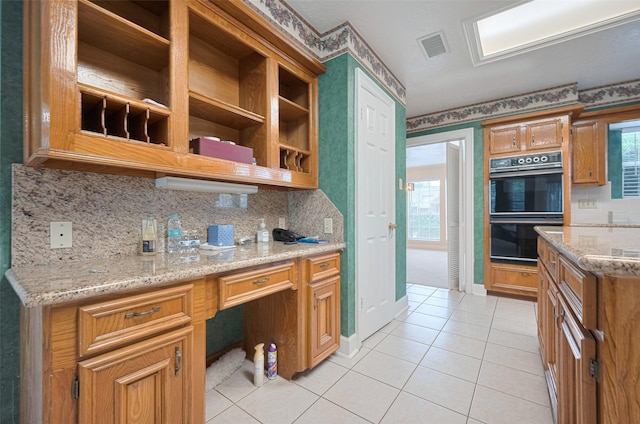 kitchen featuring backsplash, light tile patterned floors, light stone counters, brown cabinets, and open shelves