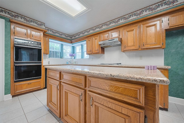 kitchen featuring under cabinet range hood, light tile patterned flooring, baseboards, and light stone countertops