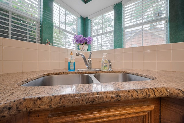 kitchen view of a sink, light stone counters, and tasteful backsplash