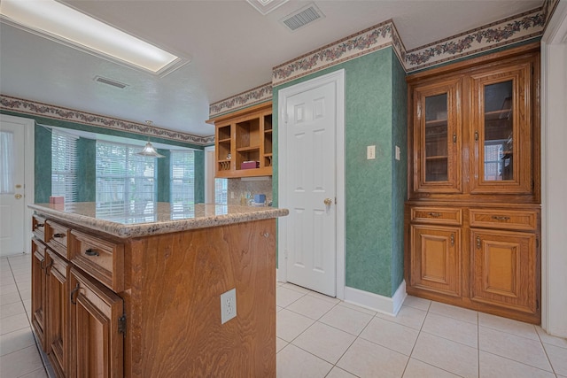 kitchen with light tile patterned floors, brown cabinetry, light stone countertops, and a center island