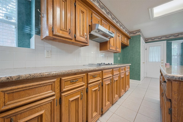 kitchen featuring under cabinet range hood, light tile patterned floors, brown cabinetry, and plenty of natural light