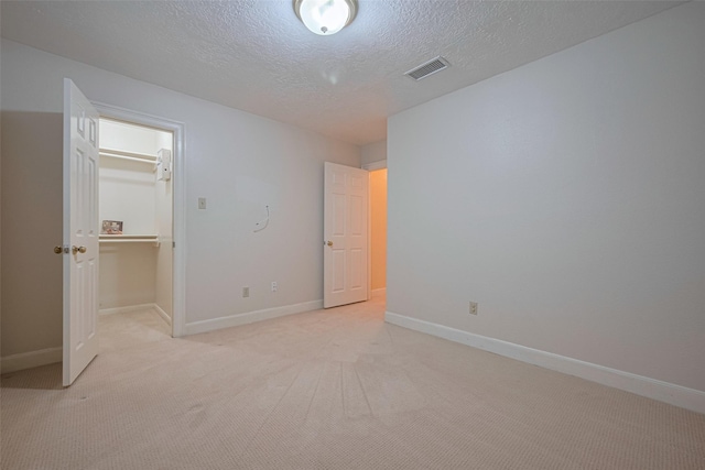 unfurnished bedroom featuring a textured ceiling, light carpet, baseboards, a walk in closet, and a closet