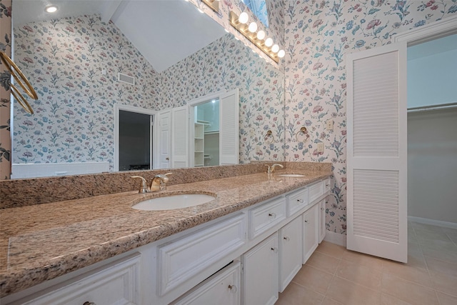 full bathroom with wallpapered walls, double vanity, vaulted ceiling, tile patterned flooring, and baseboards