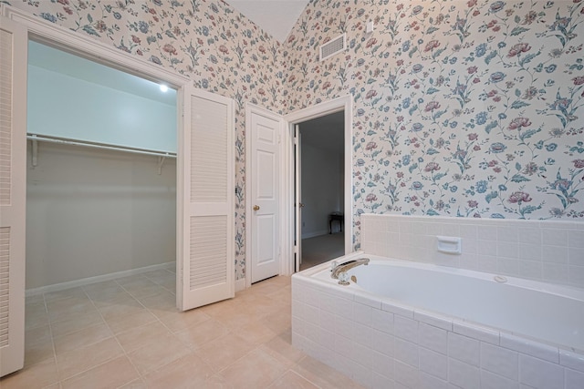 bathroom with wallpapered walls, a garden tub, a walk in closet, tile patterned flooring, and baseboards