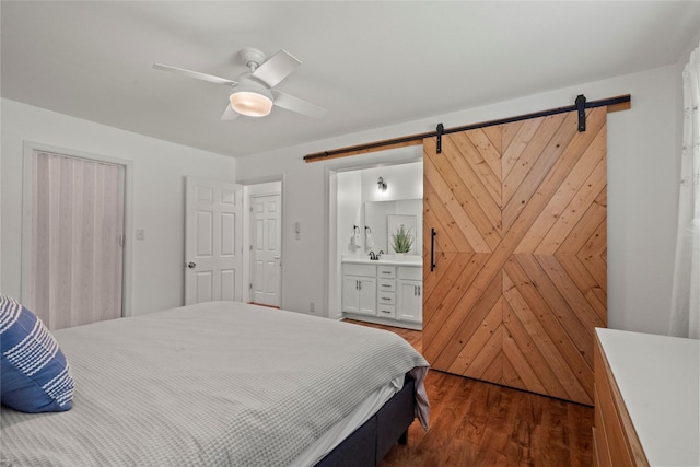 bedroom with a barn door, dark wood-style flooring, ensuite bathroom, and a ceiling fan