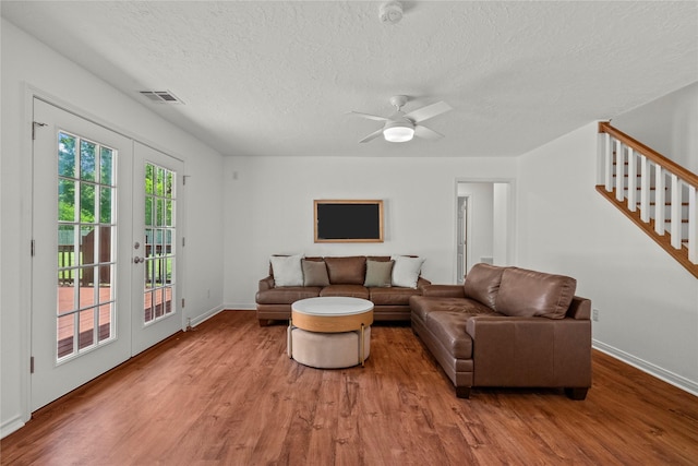 living room featuring a textured ceiling, wood finished floors, stairs, baseboards, and ceiling fan