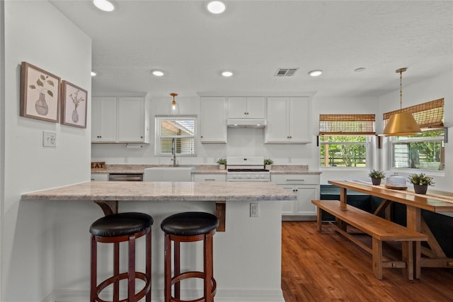 kitchen with white stove, a sink, a breakfast bar, white cabinetry, and recessed lighting