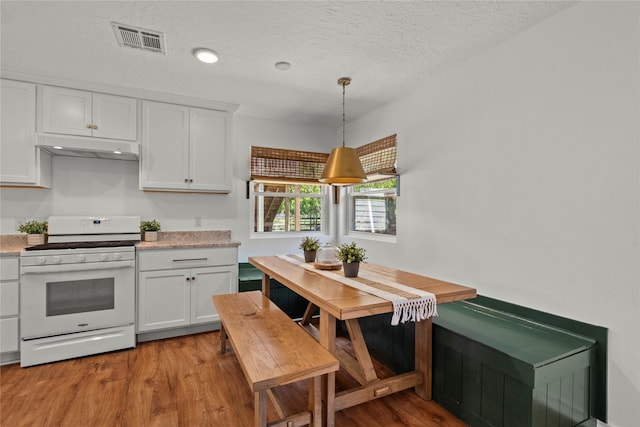 kitchen featuring white range with gas cooktop, under cabinet range hood, white cabinets, wood finished floors, and a textured ceiling