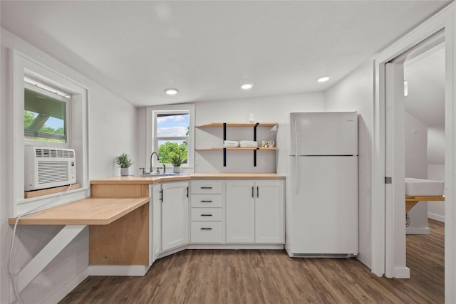 kitchen with freestanding refrigerator, a sink, wood finished floors, white cabinetry, and baseboards