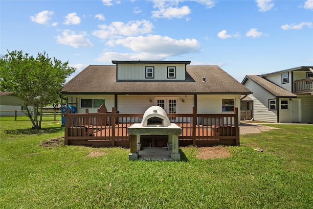 rear view of property with a deck, a yard, roof with shingles, and an outdoor fire pit