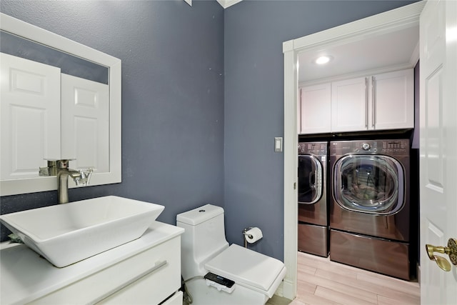clothes washing area with washing machine and clothes dryer, cabinet space, and light wood-style floors