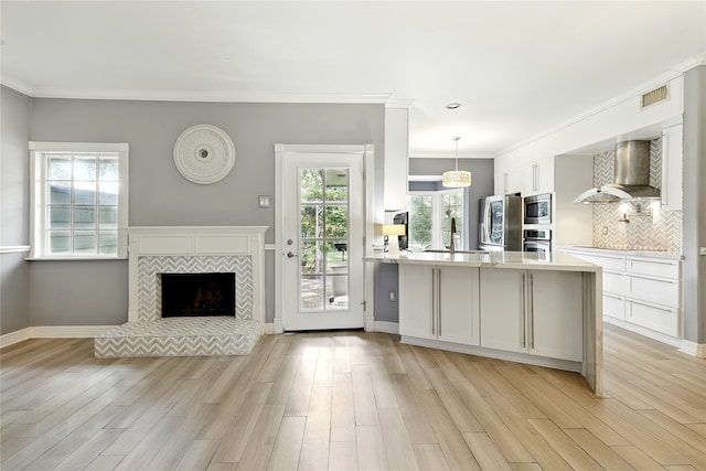 kitchen featuring wall chimney exhaust hood, stainless steel appliances, a sink, white cabinetry, and light countertops