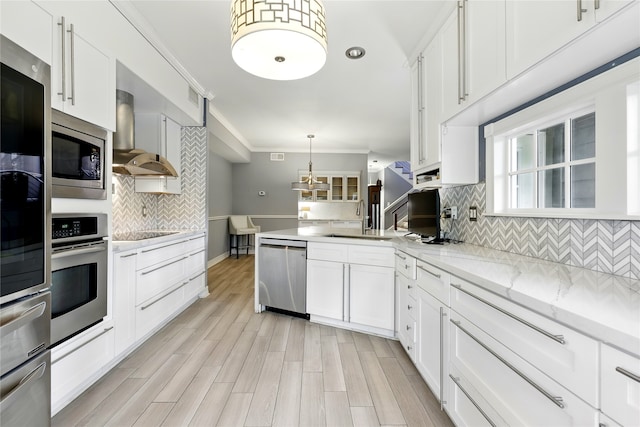 kitchen with appliances with stainless steel finishes, a sink, a peninsula, backsplash, and ornamental molding