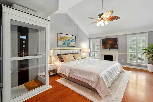 bedroom featuring wood finished floors, multiple windows, lofted ceiling, ornamental molding, and a fireplace