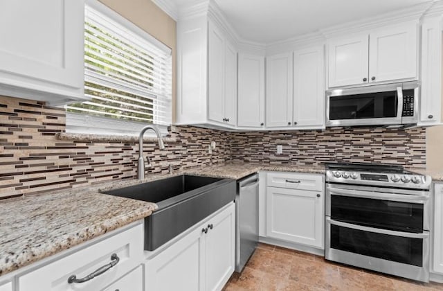 kitchen with appliances with stainless steel finishes, white cabinets, a sink, decorative backsplash, and light stone countertops