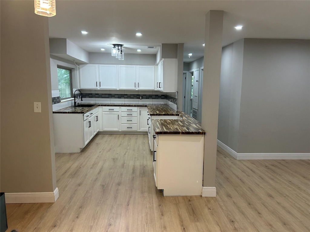 kitchen with baseboards, light wood-style floors, a sink, white cabinetry, and tasteful backsplash