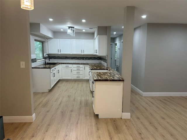 kitchen with baseboards, light wood-style floors, a sink, white cabinetry, and tasteful backsplash