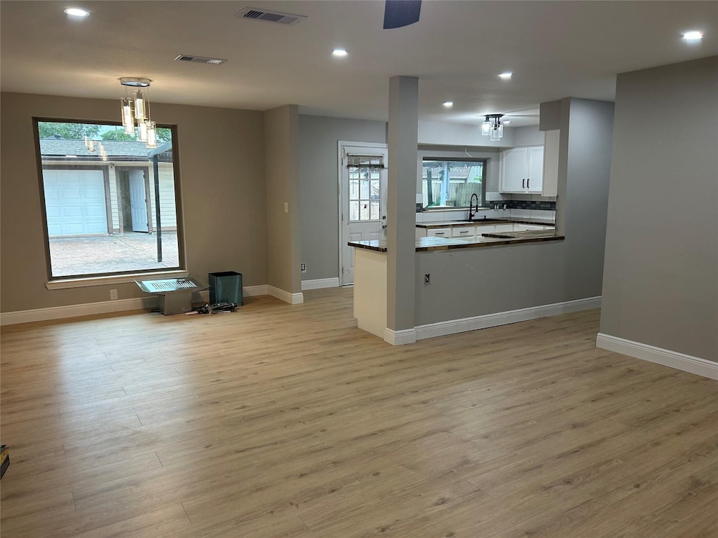 unfurnished living room featuring healthy amount of natural light, light wood finished floors, a sink, and recessed lighting