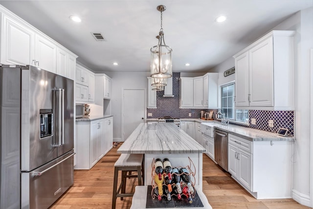 kitchen featuring appliances with stainless steel finishes, tasteful backsplash, white cabinets, light stone countertops, and recessed lighting